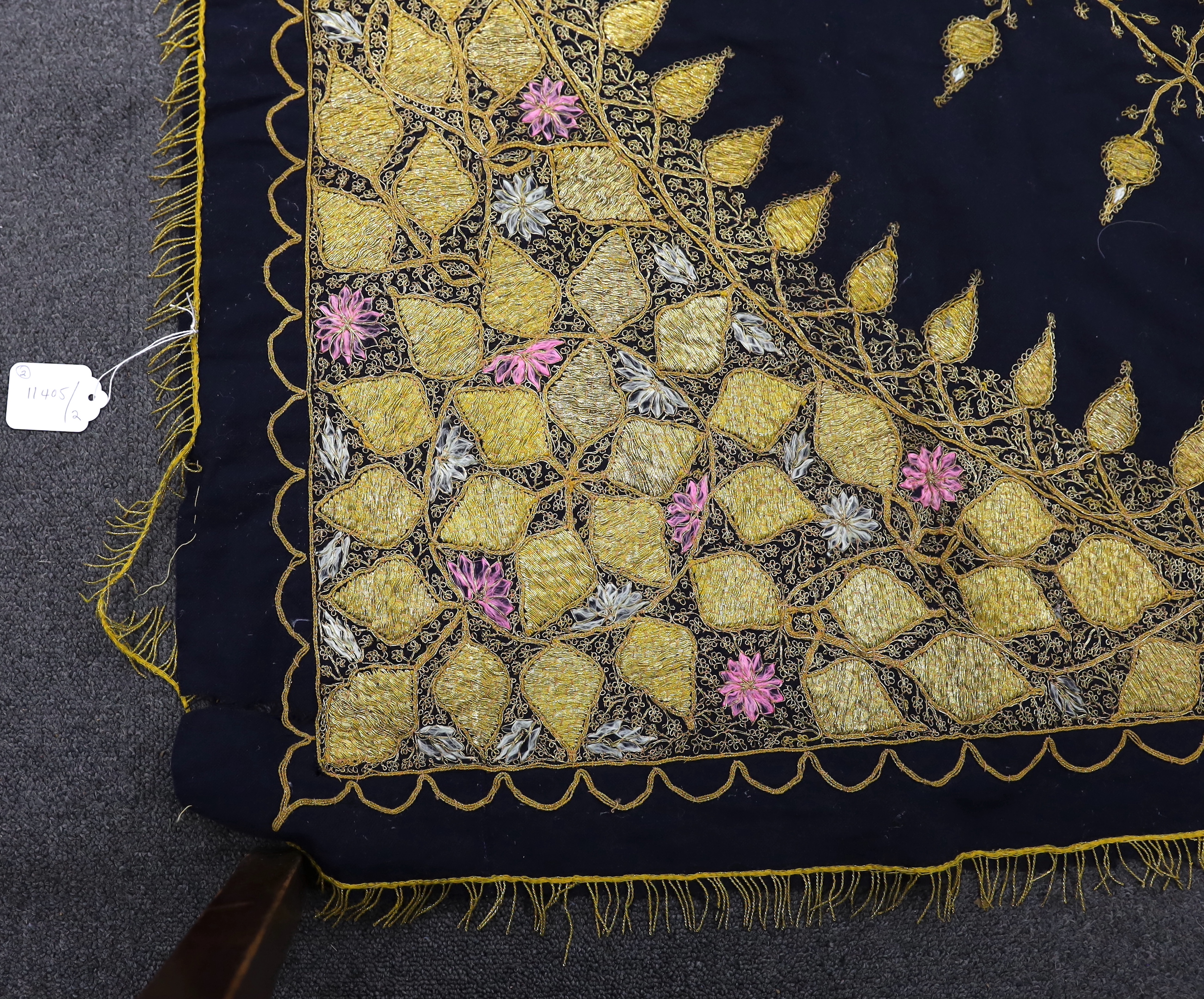 An Indian gold thread and coloured silk floss embroidered black wool cover with gold thread fringing and a later woven cover with bobble edging, black and gold cover 172cm x 169cm